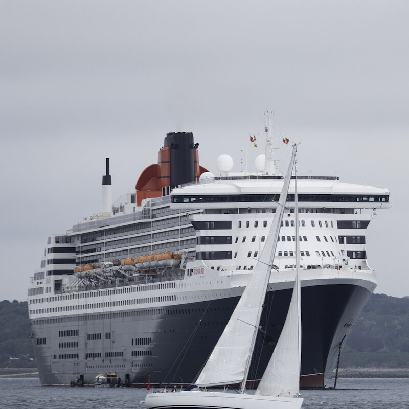 Queen Mary 2 mit Segelboot in Landnähe