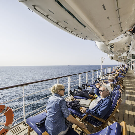 Gäste in Liegestühlen auf dem Seitendeck der Queen Mary 2